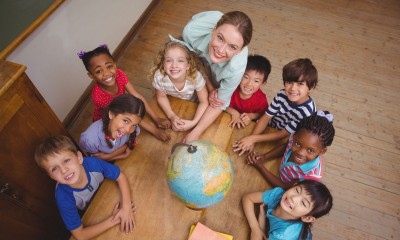 46212807 - cute pupils smiling around a globe in classroom with teacher at the elementary school